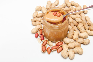 Creamy peanut butter in glass jar, peanut and spoon isolated on white background. A traditional product of American cuisine