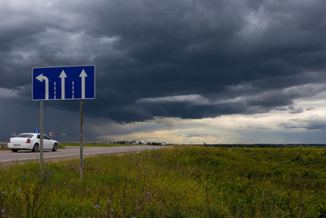 Road sign of the direction of movement against the sky with dark rain clouds. Choosing a path.