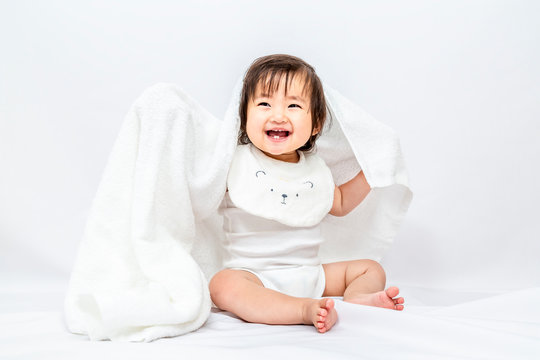 白背景で白いバスタオルを被り遊ぶ女の子の赤ちゃん。幸せ,愛情,赤ちゃん,育児イメージ