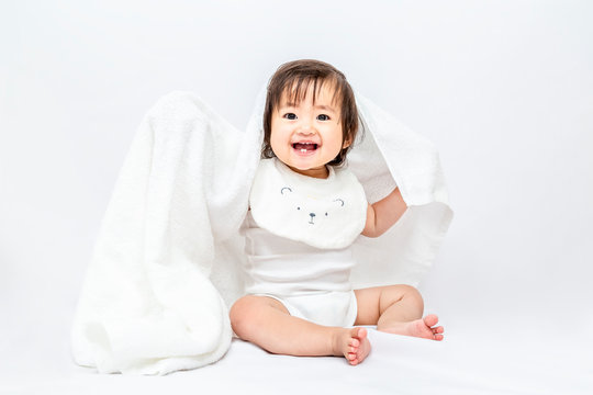 白背景で白いバスタオルを被り遊ぶ女の子の赤ちゃん。幸せ,愛情,赤ちゃん,育児イメージ