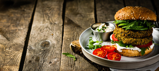 Vegan zucchini burger and ingredients on rustic wood background, copy space - obrazy, fototapety, plakaty