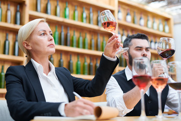 Female sommelier and her colleague in formalwear looking at wine in bokals