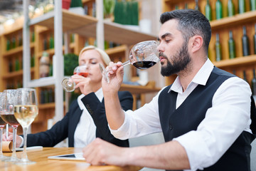 Young male sommelier smelling red wine in bokal