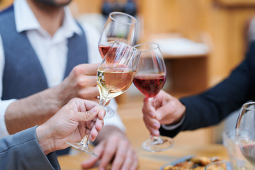 Three humans clinking with wineglasses of varoius sorts of wine