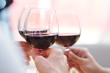 Three wineglasses with red cabernet held by toasting friends