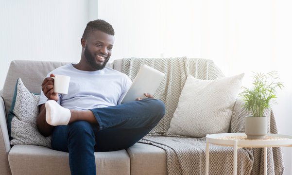 African-american millennial guy reading news on tablet and having coffee