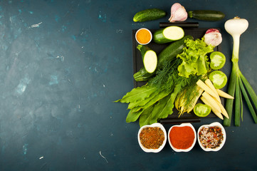THE VEGETABLES IN THE BOX ON THE STONE A DARK BACKGROUND. YOUNG GREENS ONION GARLIC ZUCCHINI BRIGHT SPICES LAY IN A WOODEN TRAY WITH HANDLES ON A DARK TEXTURED BACKGROUND.