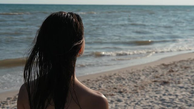 Young relaxed beautiful woman with wet brunette hairl ooking on the sea waves in slow motion, Close up
