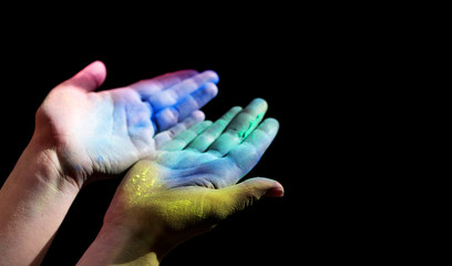 Colorful holi painted woman hands open for light on black