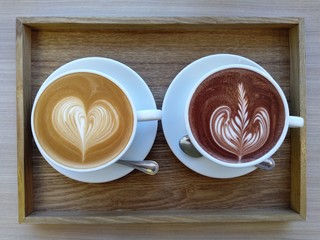 Hot latte and cocoa in white cups on the wood table at the coffee shop. Latte art coffee.