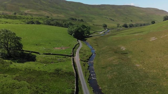 A descending aerial shot of Barbon Beck, Carnforth, Lancashire, England. This stunning countryside features a stream running alongside a small country lane.