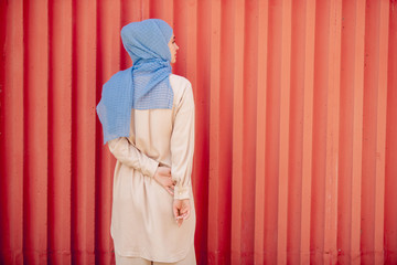 Back view of young muslim female in blue hijab and light beige casualwear
