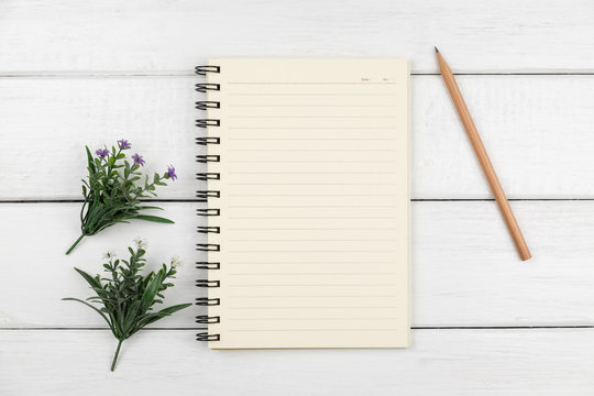 Top view of an open notebook with pencil on white wooden desk