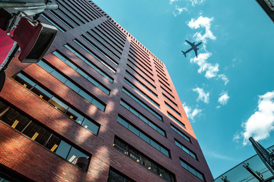 Modern Office Apartment Building With Airplane Flying Overhead In Blue Sky And Clouds