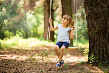 Happy Little girl on a swing in the summer park