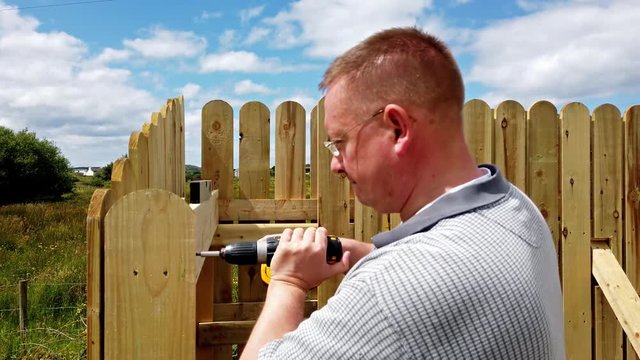 Drilling a screw into the wooden fence
