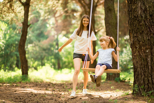 happy mother pushing laughing daughter on swing in a park