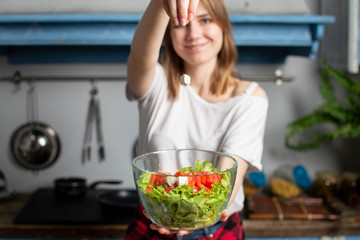young girl prepares a vegetarian salad in the kitchen, she throws pieces of cheese on a plate, the...