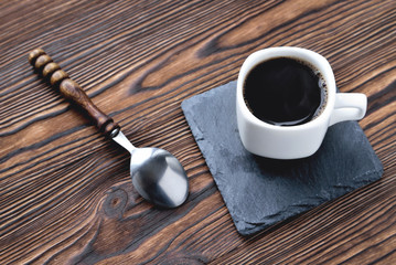 white cup with coffee on a stone stand, vintage coffee spoon, wooden natural background close up...