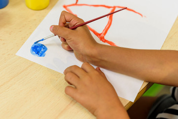 Girl painting on a white sheet with brush and colored paints: red, yellow, brown and blue. Children's crafts. Back to school.