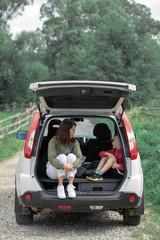 young mother with kid boy sitting in car trunk resting in summer sunny day