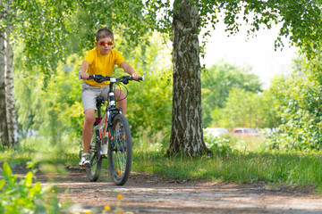Naklejka premium A boy wearing sun glasses riding a bike along a park alley