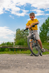Fototapeta na wymiar Portrait of a boy in sunglasses, with a bicycle, against a background of trees and blue sky