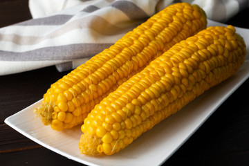 Boiled corn on a white plate on a dark wooden table. Close-up