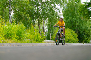 Naklejka premium Teenager rides through the park on a bicycle
