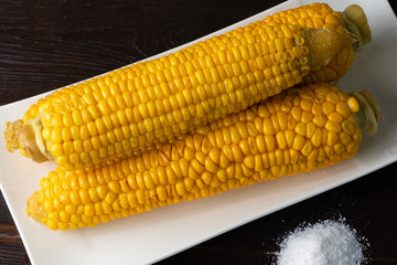 Boiled corn on a white plate on a dark wooden table. Close-up