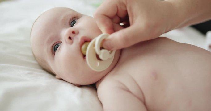 Restless newborn baby wriggling in a cot as the mother inserts a dummy which the child spits out trying to put a thumb in its mouth