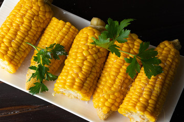 Boiled corn on a white plate on a dark wooden table. Close-up