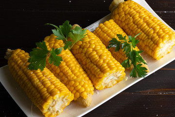 Boiled corn on a white plate on a dark wooden table. Close-up
