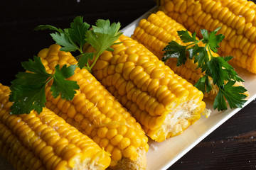 Boiled corn on a white plate on a dark wooden table. Close-up