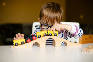 little ginger child boy in the glasses with syndrome dawn playing with wooden railways