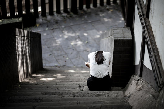 A girl is sitting down on the stair. She seem to be sadly, cry or stress with some problem. Selected focus on back of body. Abstract and stress emotional concept photo.