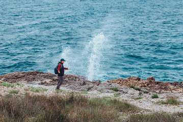 man walking by rocky sea beach in windy weather