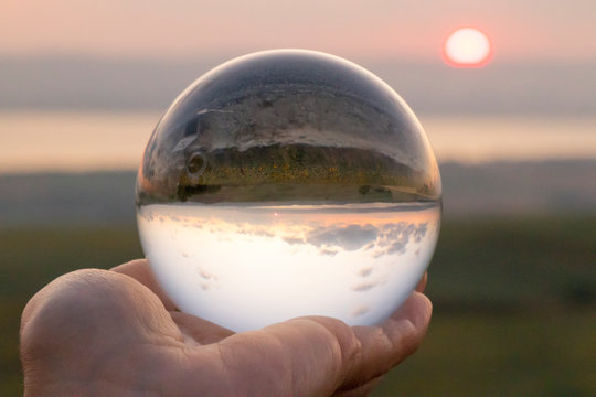 Crystal ball photography - sunset nature landscape, hand holding the ball