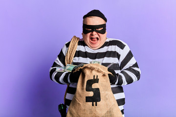 cruel guilty thief holding a sack and loking at the camera. isolated blue background. studio shot.profitable deal.