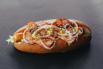 Big hotdog with sausage tomatoes, mustard and salad isolated on black background.