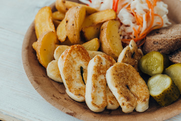 Tasty grilled fish with fried potatoes, cucumber, cabbage and woods in a paper plate on a wooden table. takeaway street food