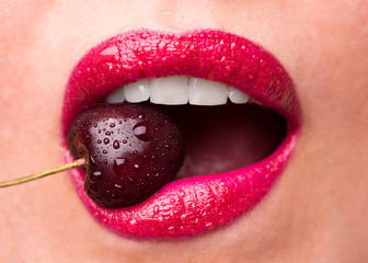Red lipstick on lips and a cherry with water droplets. The girl is eating cherry.