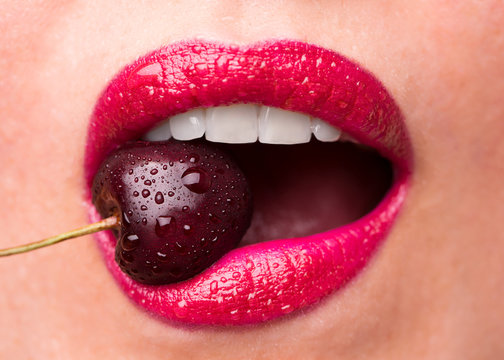 Red lipstick on lips and a cherry with water droplets. The girl is eating cherry.