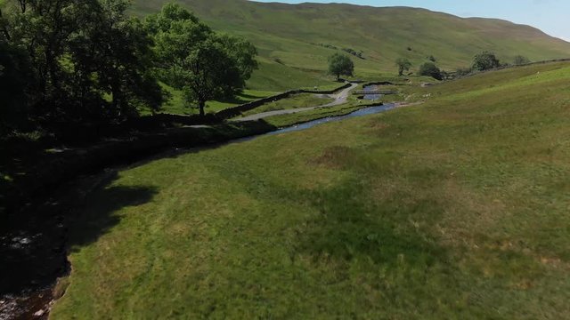 A pullback aerial shot of Barbon Beck, Carnforth, Lancashire, England. This stunning countryside features a stream running alongside a small country lane.