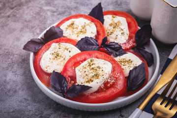 traditional Italian caprese salad, snack of tomato, mozzarella cheese, basil and spices, close-up, copy space