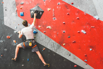 Sportsman climber moving up on steep rock, climbing on artificial wall indoors. Extreme sports and bouldering concept - obrazy, fototapety, plakaty
