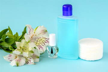 Fototapeta na wymiar Glass bottle with colorless nail polish, plastic bottle with nail varnish remover, cotton pads and white flowers on a blue background. Manicure, pedicure, nail care products.