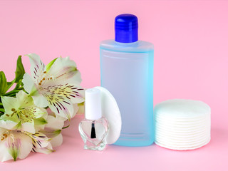 Obraz na płótnie Canvas Glass bottle with colorless nail polish, plastic bottle with nail varnish remover, cotton pads and white flowers on a pastel pink background. Manicure, pedicure, nail care products.