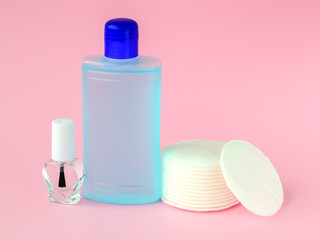 Glass bottle with colorless nail polish, plastic bottle with nail varnish remover and cotton pads on a pastel pink background. Manicure, pedicure, nail care products.