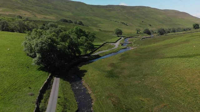 A pullback aerial shot of Barbon Beck, Carnforth, Lancashire, England. This stunning countryside features a stream running alongside a small country lane.